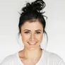Portrait of Elena Ruiz smiling in a neutral studio setting.