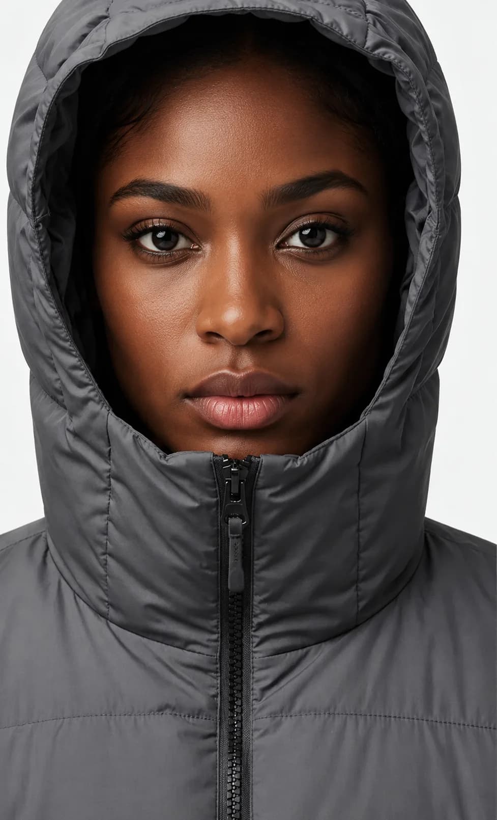 Close-up portrait of a woman in a gray hooded puffer jacket with the hood up.